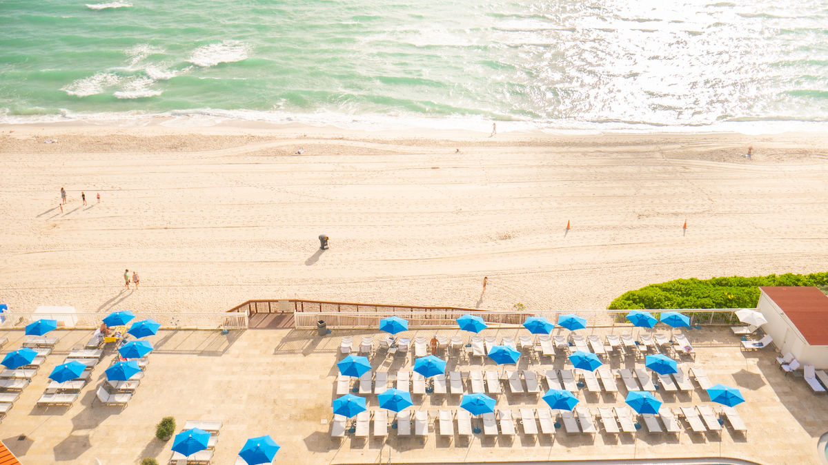 Glistening ocean water and white sand beach with blue umbrellas.